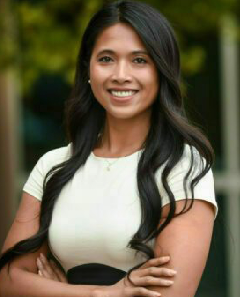 Smiling woman with long dark hair in a white top, outdoors with arms crossed.