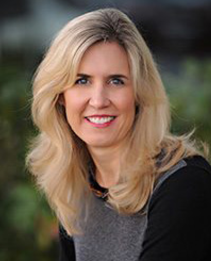Portrait of a smiling blonde woman outdoors with a blurred green background.